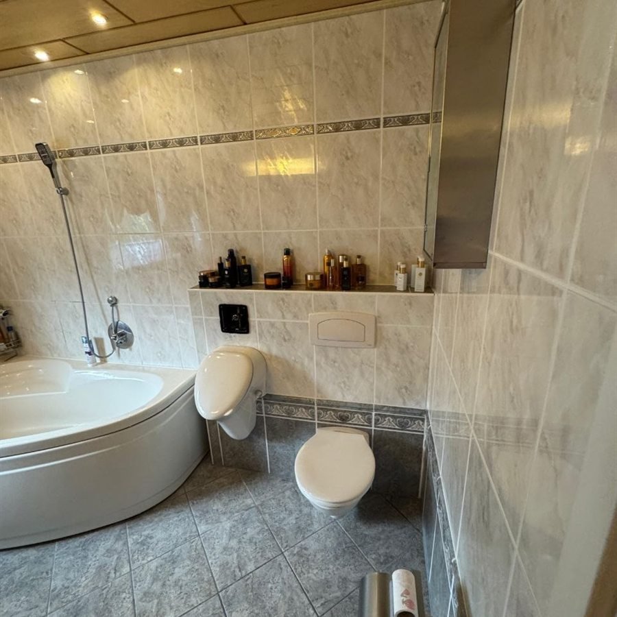 Vorher: Eckbadewanne neben WC und Urinal vor gemusterten Fliesen